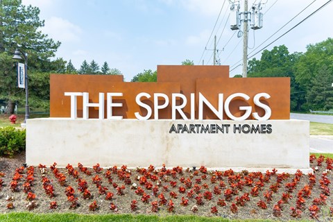 a sign for the springs apartment homes with red flowers in front of it